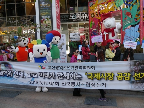 ▲지난17일과거와현재,그리고미래가함께하는“국제시장공감선거캠페인”플래카드를내걸고거리퍼레이드를펼치고있다.