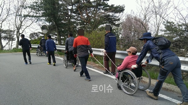 사회봉사대상자들이장애인이탄휠체어를끌고당기며함께정상을향해가고있다.(사진제공=부산준법지원센터)