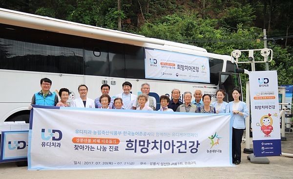 유디치과 의료진과 검진 및 치료를 받으신 어르신들이 함께 유디덴탈버스 앞에서 기념촬영을 하고 있다