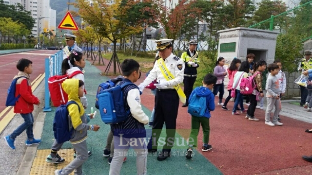 초등학생들에게 홍보물을 나눠주며 교통안전 캠페인을 벌이고 있다.