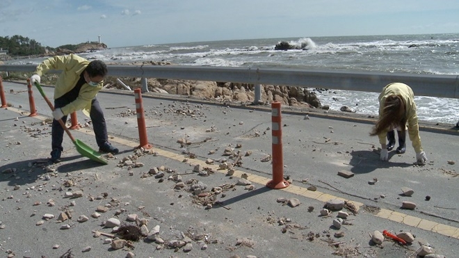 기장군 직원들이 태풍 마이삭으로 인해 대변리 해안도로에 쌓인 돌멩이들을 치우고 있다.(사진제공=부산기장군)