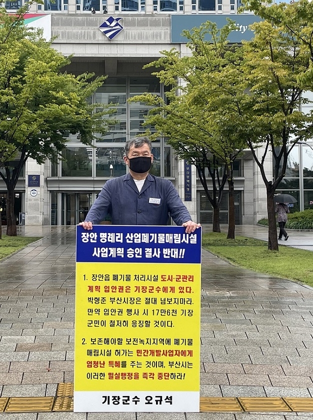 오규석 기장군수는 9월 17일 오전 11시 40분 부산시청 앞에서 장안읍 일원 산업폐기물 매립장 사업계획 결사반대를 위한 19번째 1인 시위를 빗속에서 진행하고 있다.(사진제공=부산 기장군)