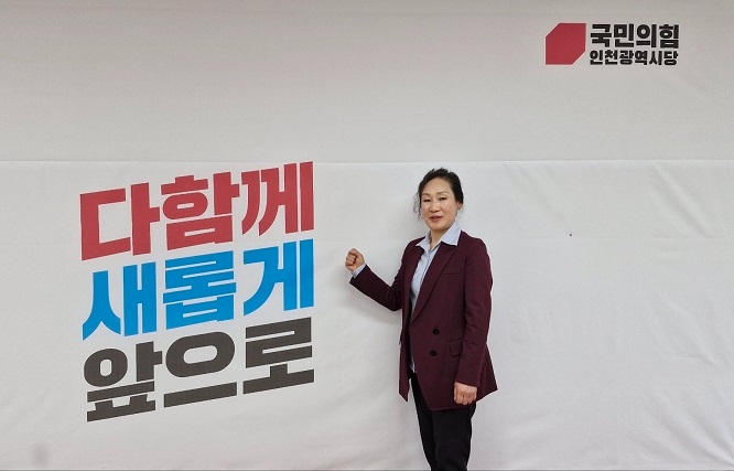 강경숙 예비후보가 국민의 힘 현수막 앞에서 주먹을 굳게 쥐고 승리를 염원하고 있다.