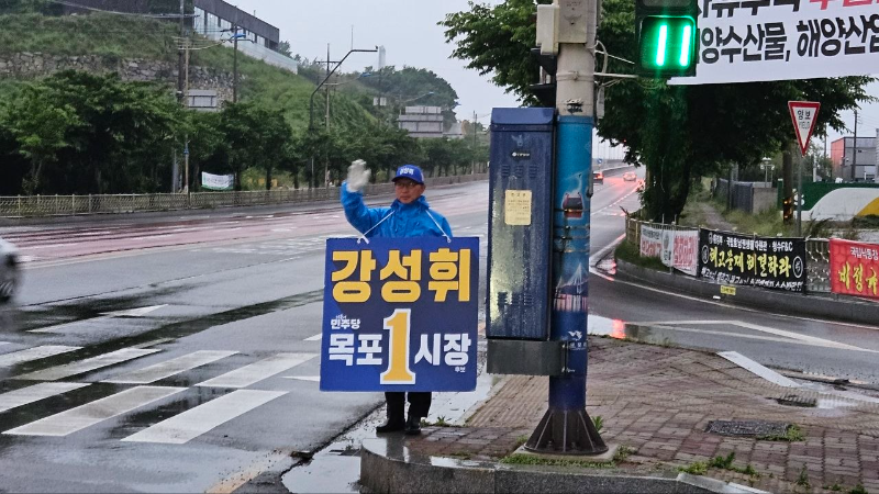 ▲강성휘 더불어민주당 목포시장 후보가 선거운동 마지막 날인 2일 오전 비가 내리는 가운데 목포대교 사거리와 행남사 사거리에서 출근길 시민들에게 인사를 하고 있다(사진=강성휘 후보실 제공)