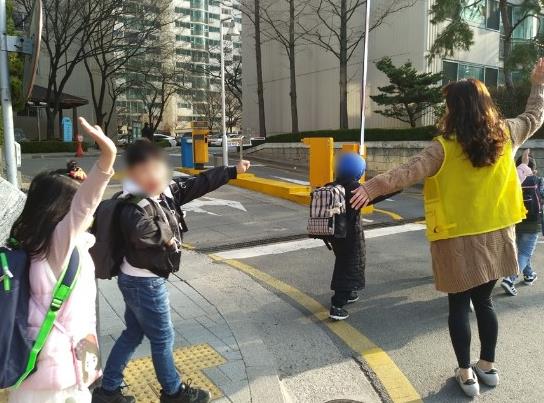 어린이들이 교통안전지도사와 함께 등교하고 있다.