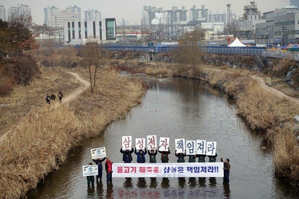 ▲수원삼성전자앞에위치한원천리천에서물고기떼죽음에대한삼성의책임을요구하는피켓시위를벌이고있다.(사진제공=다산인권센터)