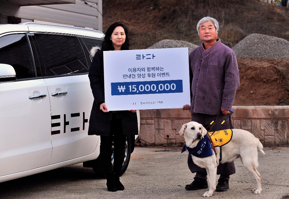 한서진 타다 마케팅본부장(왼쪽)과 이형구 한국장애인도우미견협회장(오른쪽)이 훈련 중인 시각장애인도우미견과 함께 기부금 전달식 기념사진을 촬영하고 있다.
