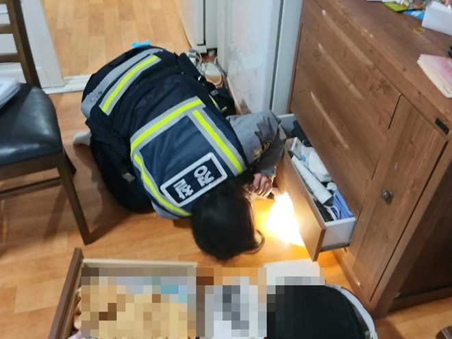 김새봄 순경이 서랍장 밑을 손전등으로 비쳐보고 있다.