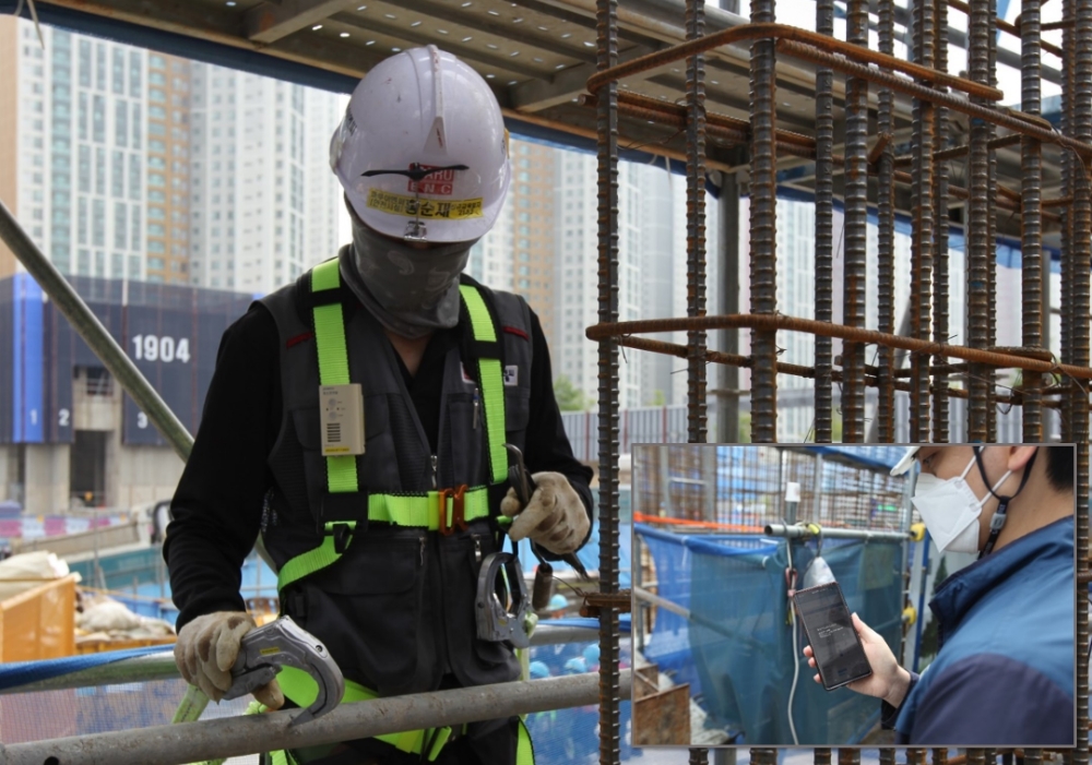 포스코건설 공사 현장에서 작업자가 스마트 안전벨트의 알람을 듣고 안전고리를 체결하고 있으며, 안전관리자는 모바일로 작업자의 안전고리 미체결 상태를 확인하고 있다.(사진=포스코건설)