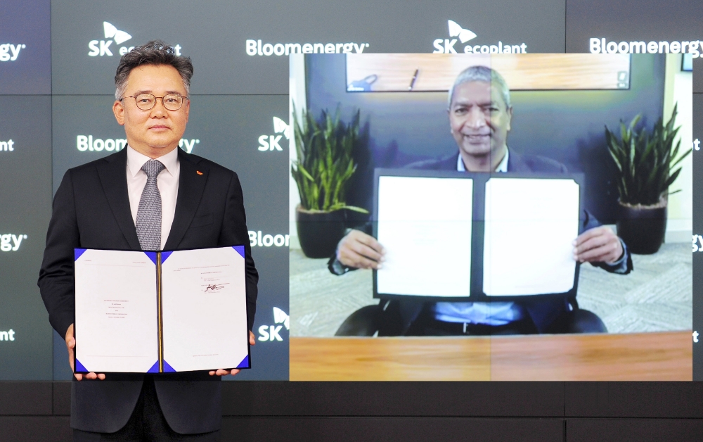 박경일 SK에코플랜트 대표이사(왼쪽)와 케이알 스리다르(KR Sridhar) 블룸에너지 창업자 겸 최고경영자(CEO)가 온라인 화상시스템을 통해 계약서를 들고 기념촬영을 하고 있는 모습.(사진=SK에코플랜트)