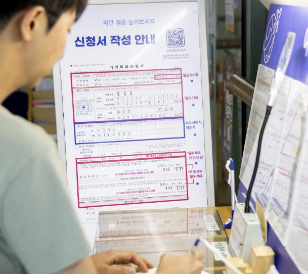 용산구민이 용산구청 3층 여권민원실에 설치된 여권민원 안내 터치스크린을 참고해 여권민원 신청서를 작성하고 있다