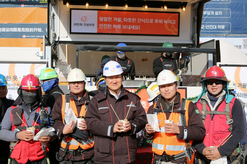 한화 건설부문 김우석 대표이사(가운데)가 건설현장 근로자들과 함께 ‘찾아가는 겨울간식차’의 호빵과 어묵을 즐기고 있다.(사진=한화 건설부문)