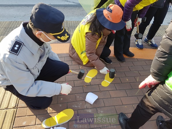 어린이 교통사고 예방을 위해 망치로 노란발자국 시트를 설치하고 있다.
