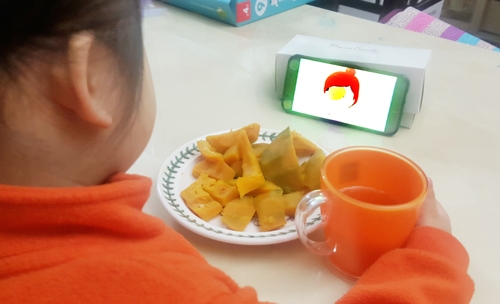 한 아이가 식사 중 스마트폰으로 동영상을 시청하고 있다.