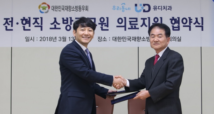 왼쪽부터 진세식 유디치과협회 협회장과 김철종 대한민국재향소방동우회 회장이 전현직 소방관들을 위한 의료지원협약서에 사인을 하고 악수를 하고 있다. (사진=유디치과)