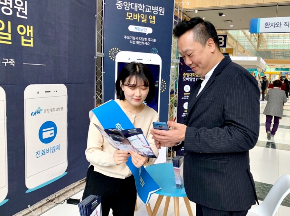 중앙대학교병원 중앙관 1층에 마련된 홍보 부스서 레몬헬스케어 관계자가 병원 이용객에게 스마트 헬스케어 플랫폼 '엠케어' 기반의 '중앙대학교병원 모바일 앱' 사용법을 안내하고 있다. (사진= 레몬헬스케어)