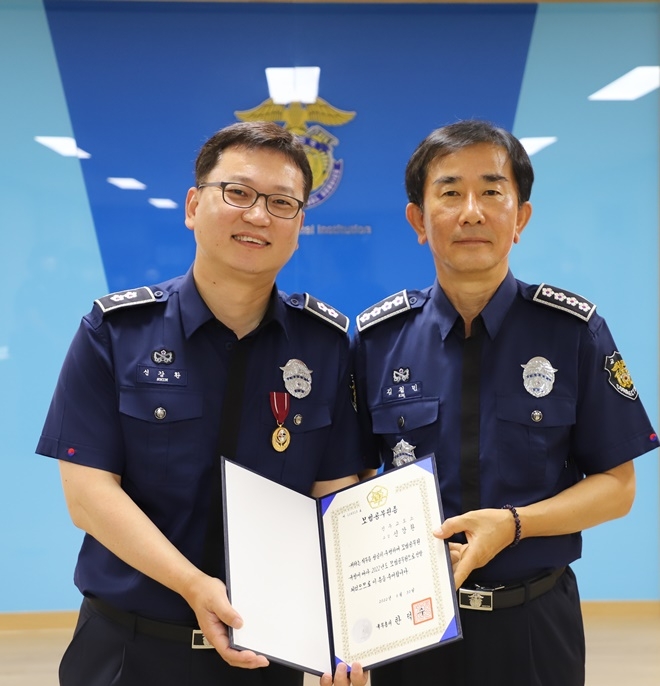 신강환 교감(왼쪽)이 모범공무원증을 내보이며 김철민 교도소장과 기념촬영을 하고 있다.(사진제공=진주교도소)