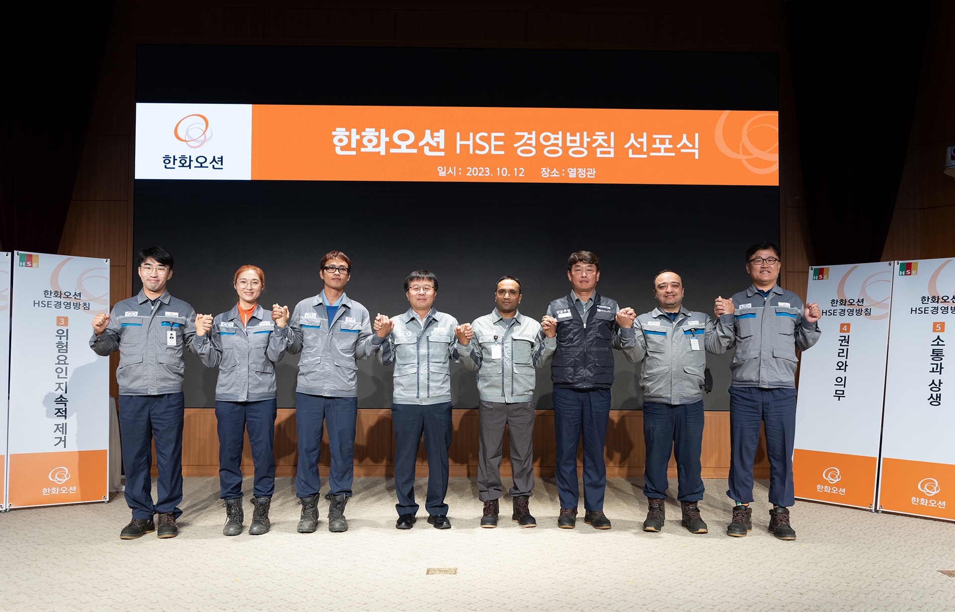 12일 거제사업장에서 진행된 '한화오션 HSE 경영방침 선포식'에서 권혁웅 대표이사(왼쪽 네번째), 정상헌 지회장(왼쪽 여섯번째)과 외국인 근로자들을 포함한 직원들이 안전 최우선 실천을 다짐하고 있다.(사진=한화오션)