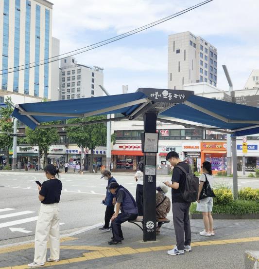 횡단보도 신호를 기다리며 스마트그늘막과 벤치를 이용하는 주민들